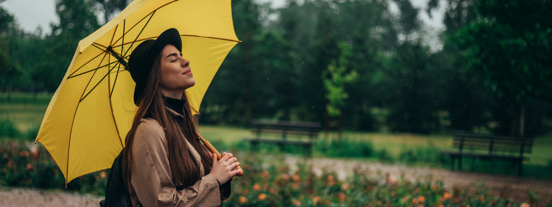 Woman with a yellow umbrella stands in the rain with her eyes closed