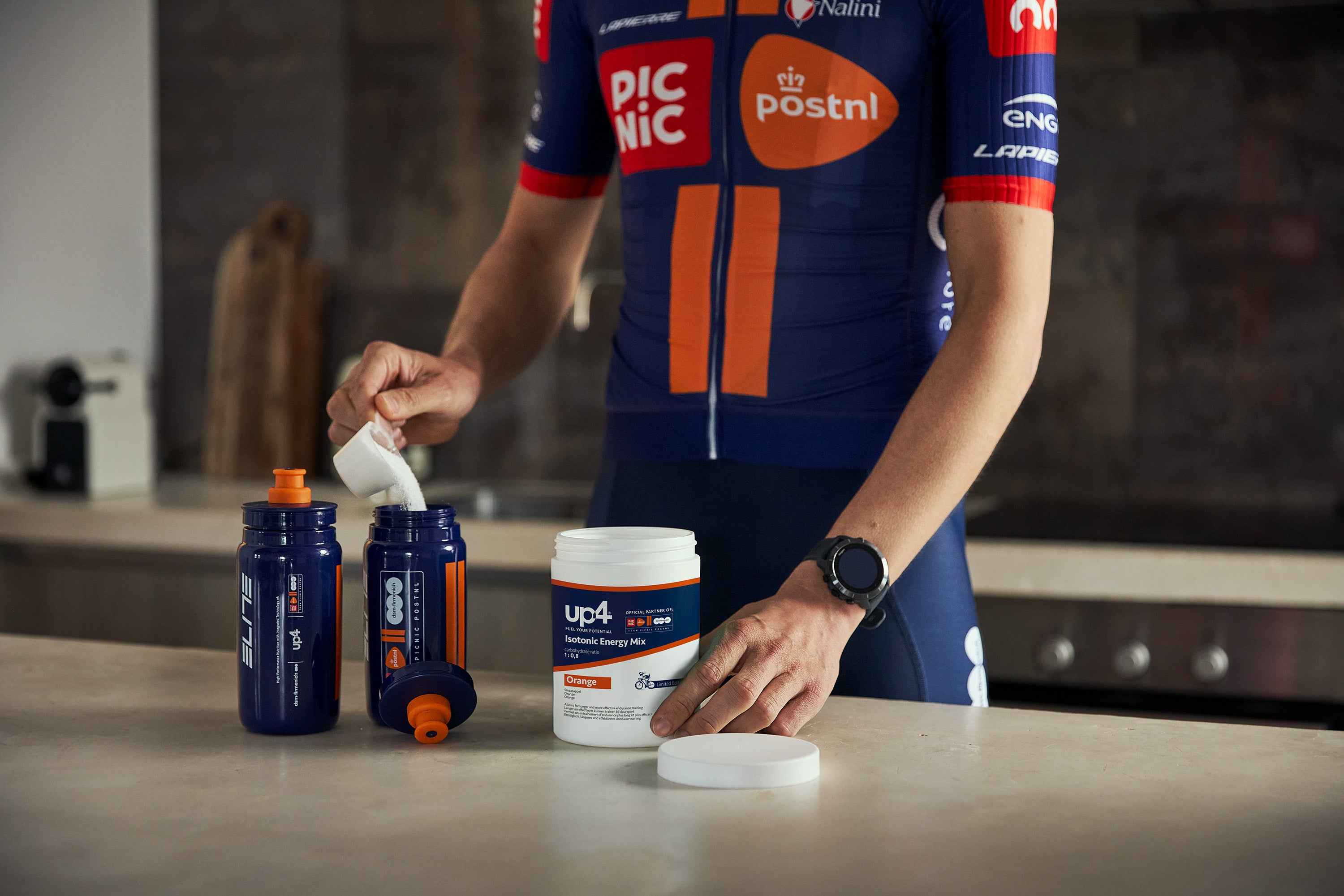 Person in a cycling jersey with sports nutrition products on a counter